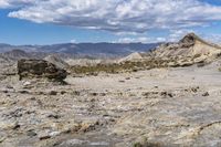 a lone motorcycle rider on rocky terrain with large rock mountains in the background with a blue sky