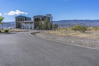 a paved road near a building with mountains in the distance on a clear day with blue sky