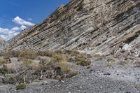 a person on a horse in front of a rocky mountain slope, with sparse vegetation