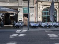 the tables outside the restaurant are covered with white table cloths and chairs set outside the building