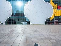 the shadow of someone on an empty tiled floor with a building in the background and large white clouds