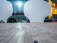 the shadow of someone on an empty tiled floor with a building in the background and large white clouds