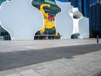 a white elephant sculpture sits in front of a large building with a large yellow bear