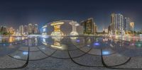 a sculpture is in the middle of a plaza with buildings in the background with lights