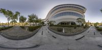 a photo taken in a fish eye lens of a building and street, with a skateboarder doing a trick