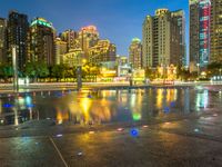 an empty sidewalk next to a large pond and tall buildings in the city skyline at night