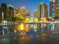 an empty sidewalk next to a large pond and tall buildings in the city skyline at night