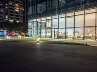 a dark street next to a light and night time building at an intersection with lots of glass