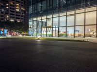 a dark street next to a light and night time building at an intersection with lots of glass