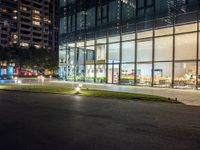 a dark street next to a light and night time building at an intersection with lots of glass