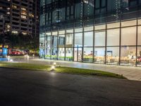 a dark street next to a light and night time building at an intersection with lots of glass