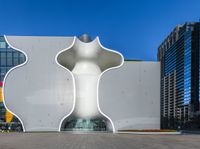 a giant white object with curved pillars sits in the middle of a stone sidewalk next to large buildings