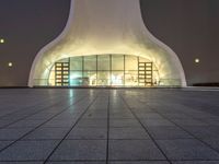 an image of a very modern building at night with lights shining around the outside of it