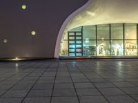 an empty space with big windows at night time and lights on above them, a red fire hydrant and white building