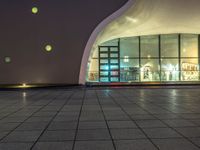 an empty space with big windows at night time and lights on above them, a red fire hydrant and white building