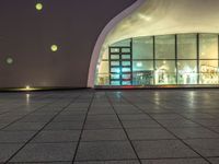 an empty space with big windows at night time and lights on above them, a red fire hydrant and white building