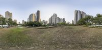 a park surrounded by tall buildings next to a green grass covered field and road next to some water