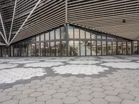 an empty concrete floor of squares in front of a building with large windows and glass