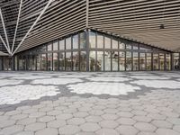 an empty concrete floor of squares in front of a building with large windows and glass