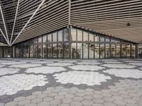 an empty concrete floor of squares in front of a building with large windows and glass