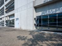 an empty road on a sunny day outside of a building with glass windows and some trees