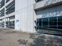 an empty road on a sunny day outside of a building with glass windows and some trees