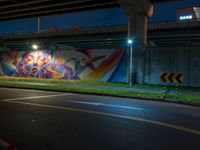 an underpass bridge next to a street at night with colorful murals on it, with a traffic sign next to the road