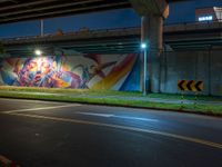 an underpass bridge next to a street at night with colorful murals on it, with a traffic sign next to the road