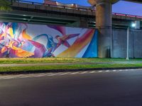 a painted mural is on a wall in front of a highway overpass in a city