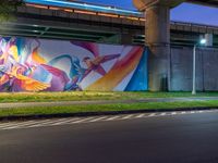 a painted mural is on a wall in front of a highway overpass in a city