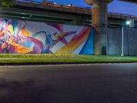 a painted mural is on a wall in front of a highway overpass in a city