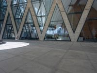 a man riding a skateboard on a cement surface in front of a building with triangular glass windows