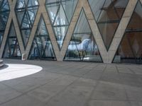 a man riding a skateboard on a cement surface in front of a building with triangular glass windows