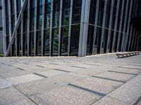 the empty street has long bars of glass around it and benches below it is surrounded by pebbles