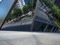 a city street reflecting in glass next to buildings on either side of it, with trees, bushes, and trees to the right