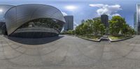 a fish - eye view of the building next to the tree lined plaza on a sunny day