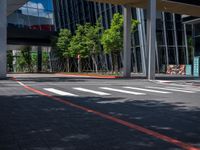 the crosswalk at a city intersection in a big modern building, with trees and some buildings around