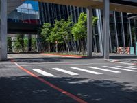 the crosswalk at a city intersection in a big modern building, with trees and some buildings around