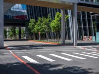 the crosswalk at a city intersection in a big modern building, with trees and some buildings around