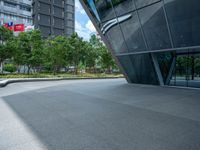 a paved square with several trees near the building's entrance and people walking along the walkway