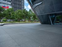 a paved square with several trees near the building's entrance and people walking along the walkway