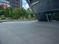 a paved square with several trees near the building's entrance and people walking along the walkway