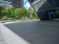 a paved square with several trees near the building's entrance and people walking along the walkway