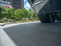 a paved square with several trees near the building's entrance and people walking along the walkway