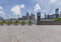 a rooftop area with cement boxes and green planters in the foreground, against a background of skyscrapers