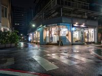 an outdoor cafe sits on a city street at night time with rain falling from the windows