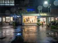 a store front with windows lit up in front and people walking out the front, outside