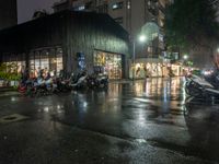 motorcycles parked next to each other on a rainy street corner in front of a building