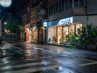 a store front with multiple plants and potted plants in the windows at night time