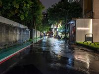 a wet street at night with street lights on and an empty bench at the end